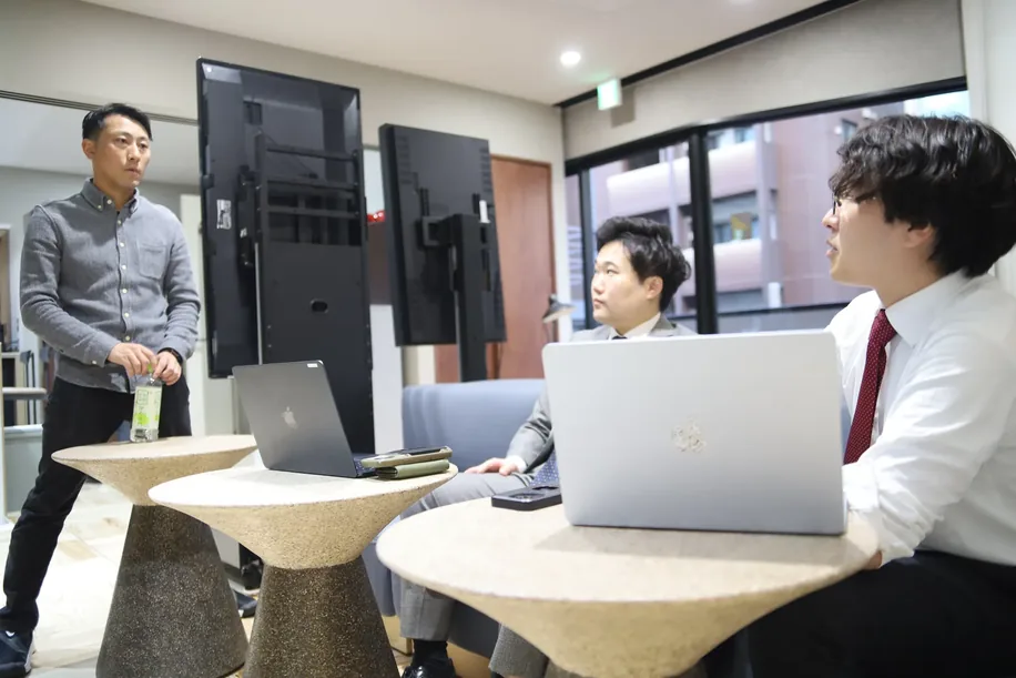 モニターの前で立って話すメンバーと、ノートPCに向かうメンバー