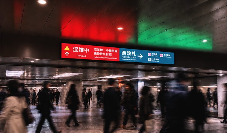 コンコースの改札振り分けサイネージと通行する乗降客（JR新宿駅）