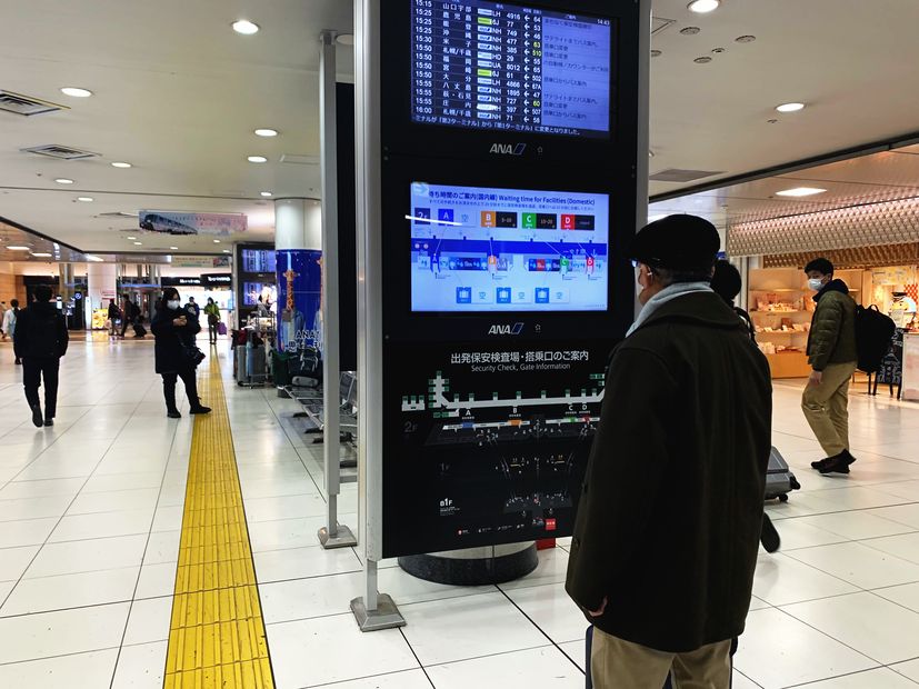 空港コンコースの待ち時間案内サイネージと旅客（羽田空港）