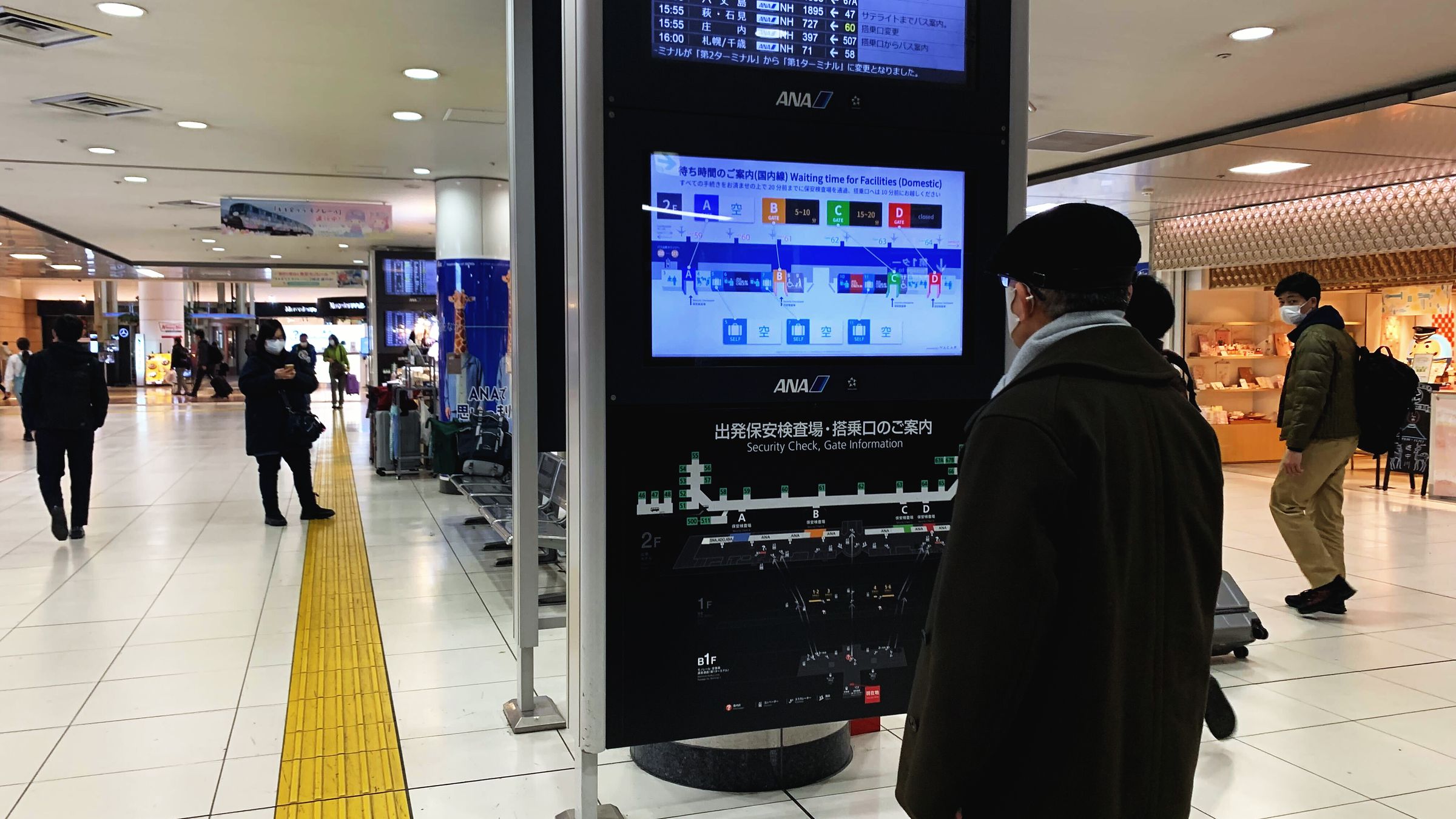 空港コンコースの待ち時間案内サイネージと旅客（羽田空港）
