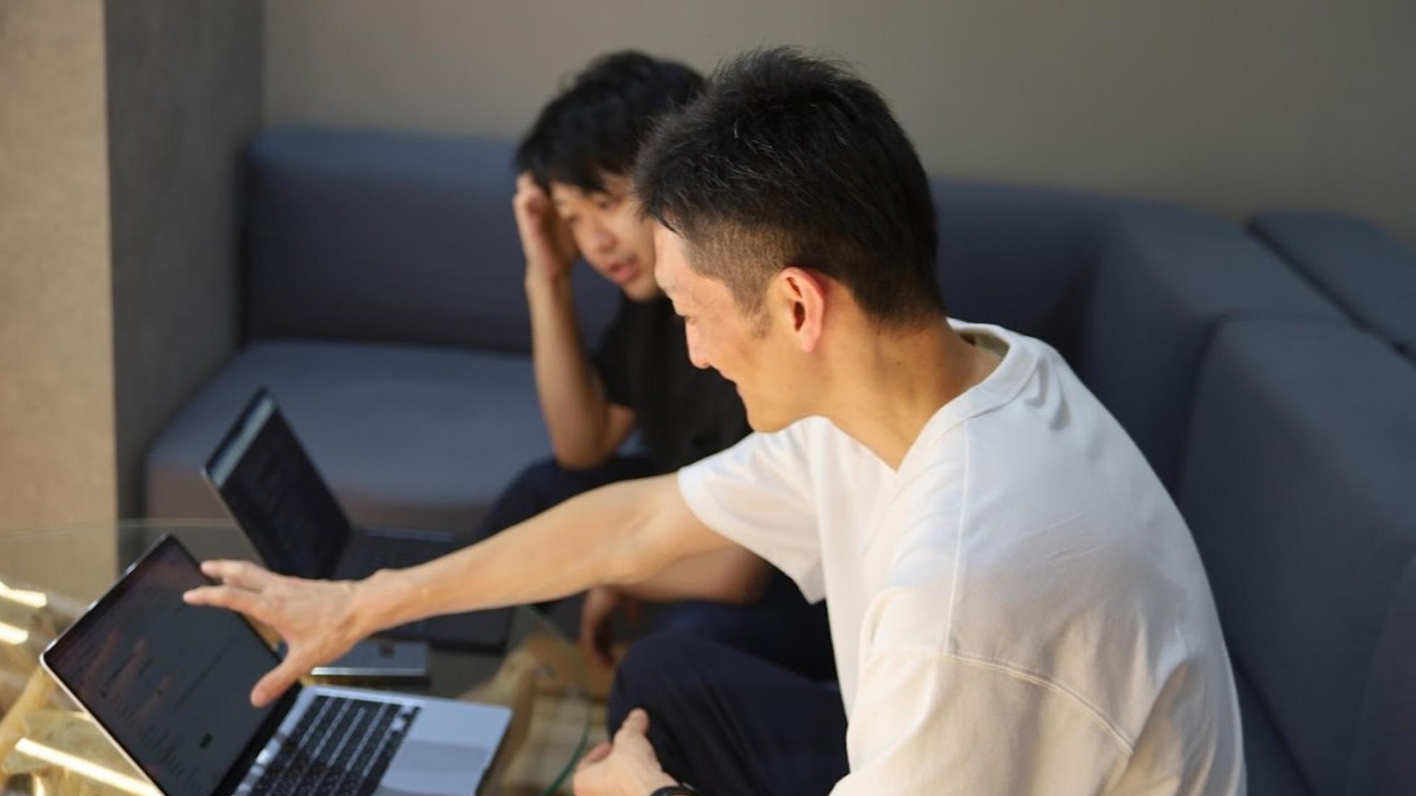 ソファに座った2人のメンバーが、ノートPCの画面を見ながら議論している様子