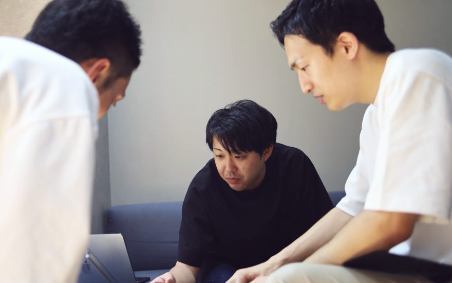 ノートPCの画面を3人で覗き込む様子